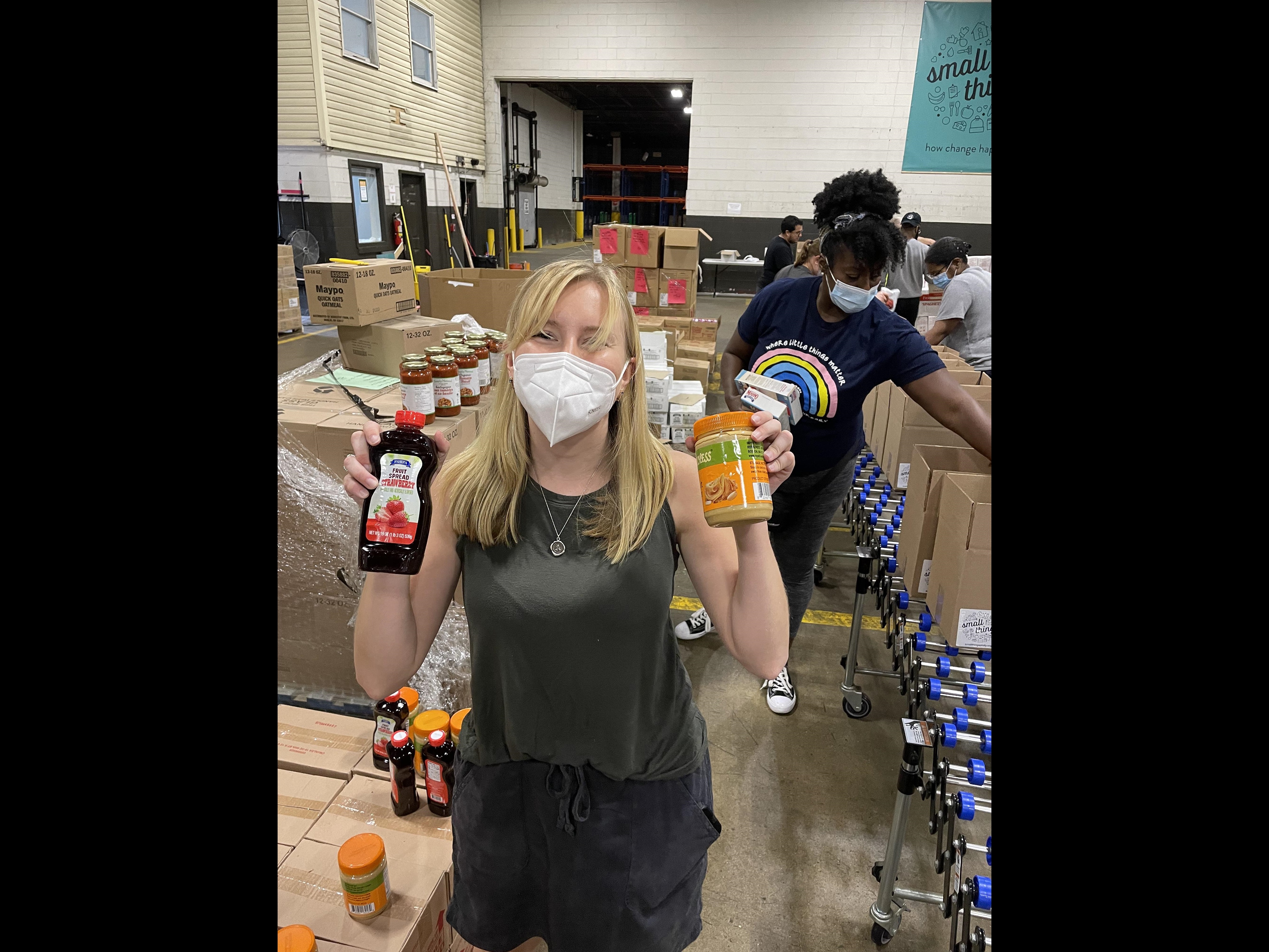 Woman in mask holding peanut butter and jelly at box packing event